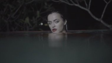 Güzel baştan çıkarıcı kadın gece açık havuzda kırmızı elbise giyiyor.