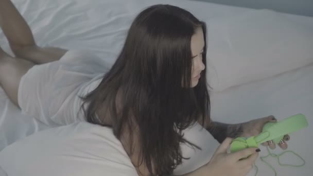 Krásná mladá brunetka žena ležící na posteli pomocí svého smartphonu a sluchátek