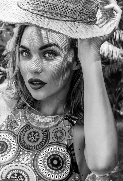 Portret van mooie vrouw dragen Bikinitop en het houden van stro hoed in haar hand op een zonnige dag op zoek naar de camera over palmbomen achtergrond. Zwart-wit foto-ogen close-up van mooi meisje met stro hoed patroon schaduw op haar gezicht — Stockfoto