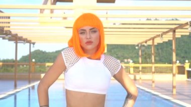 Çatı havuzu tarafından güneşli yaz gün boyunca poz modern futuristik tarzı seksi güzel kadın portre portre. Dövmeli kadın beyaz bikini ve turuncu peruk - ağır çekim video yaratıcı görünümünü