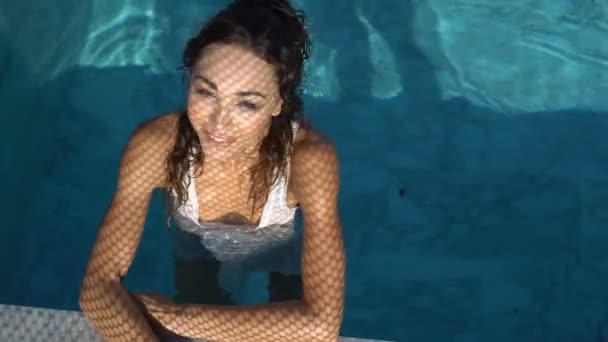 Closeup portrait of beautiful happy brunette woman posing and smiling in the outdoor swimming pool during sunny summer day with shadow net reflection on her face and body — Stock Video