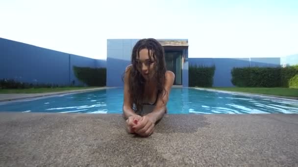 Mulher morena linda em biquíni preto elegante posando e olhando para a câmera na piscina na luxuosa villa durante o dia ensolarado de verão — Vídeo de Stock