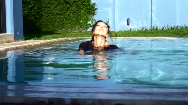 Belle femme brune se relaxant dans la piscine extérieure pendant la journée ensoleillée d'été - vidéo au ralenti — Video