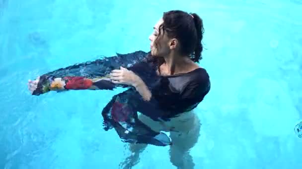 Video in alto di una bella donna bruna che indossa una tunica fiorita nera in posa nella piscina all'aperto durante la soleggiata giornata estiva — Video Stock