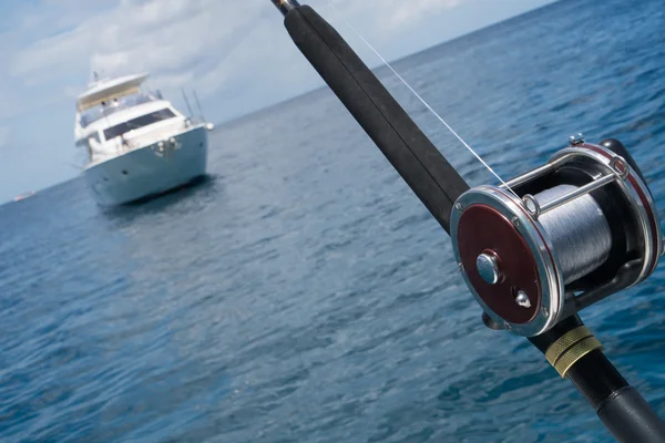 Fishing rod on a boat over blue sky and white sailing boat in the sea. Picture of fishing rod in pole holders on the back of a boat