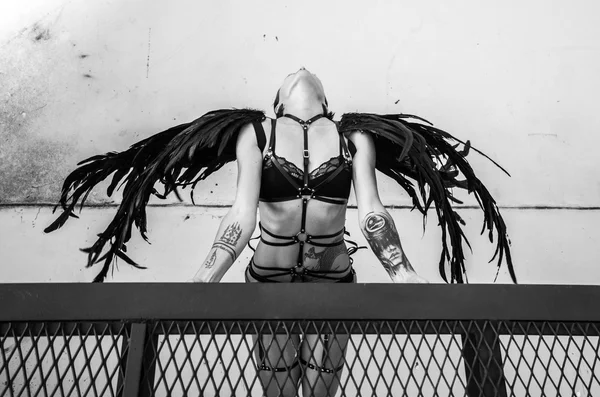 Top view black and white photo of beautiful seductive angel woman wearing lingerie and leather belts on the roof over white wall — Stock Photo, Image