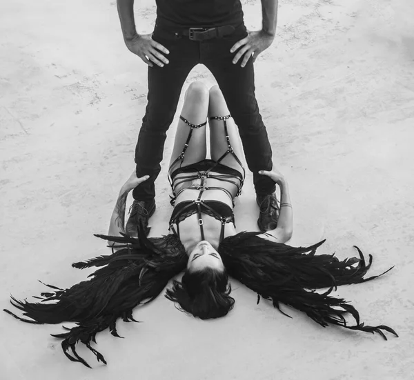 Black and white photo of romantic scene with man's silhouette standing above sensual angel woman wearing lingerie, leather belts and high heels lying on the floor — 스톡 사진