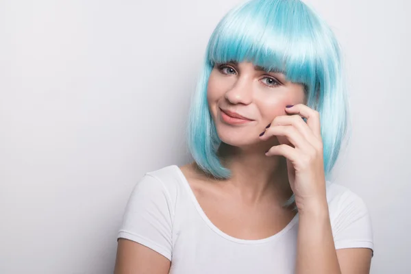 Cheeky young girl in modern futuristic style with blue wig smiling and looking into the camera over white wall background with copyspace — Stock Photo, Image