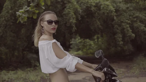 Vrij natuurlijk uitziende vrouw op zomerdag in Boho stijl mode dragen van wit overhemd, bikini en zonnebril op scooter over groene bladeren bomen achtergrond — Stockfoto