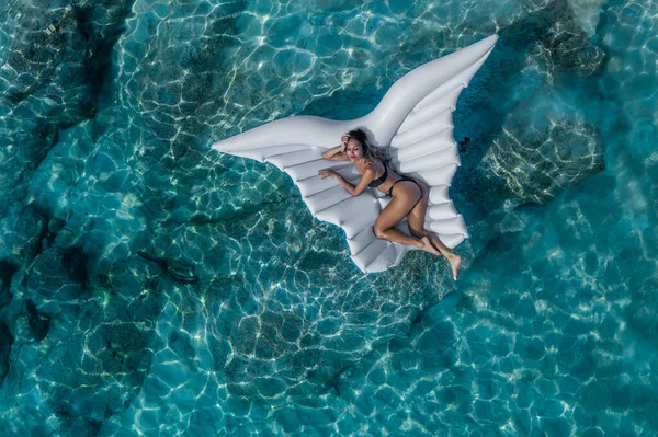 透明なターコイズブルーの海のインフレータブル翼で泳いでいる若い日焼けした女性の空中ビュー トップビューのスリム女性リラックスオン彼女の休日 — ストック写真