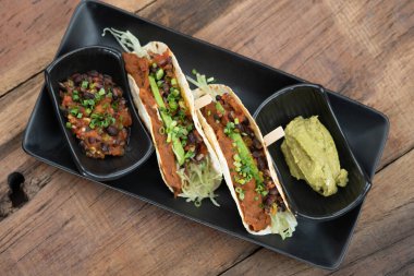 Fırında fasulye, domates, kişniş, kırmızı soğan, avokado ve yanında avokado sosu ile servis edilen çeşitli baharatlar.