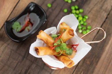 Pilav kağıdına sarılmış tavuk patates, yeşil bezelye, soğan yanında da ahşap masa üzerine izole edilmiş acı biber sosu.