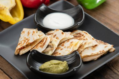 Tavuk, biber, kırmızı soğan ve mozzarella ile kızartılmış tortilla. Tahta masaya izole edilmiş guacamole sosu ve ekşi kremayla servis ediliyor.