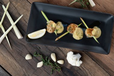 Tahta masada izole edilmiş köri karnabahar sosuyla servis edilen limon otu aromalı kavrulmuş bir Hokkaido deniz tarağı şişi.