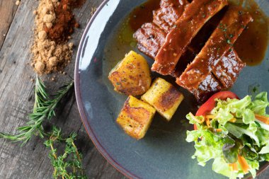 Kahverengi şeker, kimyon, füme paprika ve bbq soslu sarımsak tozu ile ahşap masada patates ve salata ile pişirilmiş yavaş pişmiş domuz eti.