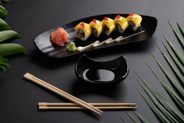 Kızarmış yumuşak kabuklu yengeç, salatalık, mango, mayonez ve tobiko tropikal yapraklarla kaplı siyah masada izole edilmiş.