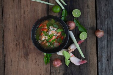 Galangal, limon otu, kaffir limon yaprağı ve ahşap masada izole edilmiş saman mantarlı geleneksel karides çorbası manzarası.