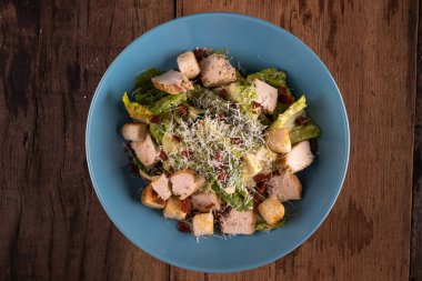 Tavuklu Cesar salatası, kızarmış ekmek ve rendelenmiş peynir ahşap kırsal masada izole edilmiş.