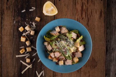 Tavuklu Cesar salatası, kızarmış peynir ve limon ahşap kırsal masada izole edilmiş.