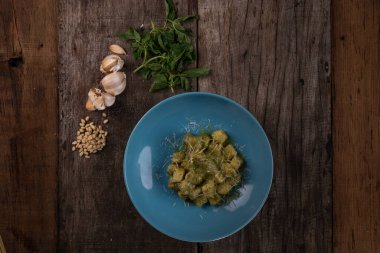 Ev yapımı pesto soslu gnocchi, parmesan ve fesleğen ahşap masada izole edilmiş.
