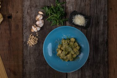Ev yapımı pesto soslu gnocchi, parmesan ve fesleğen ahşap masada izole edilmiş.