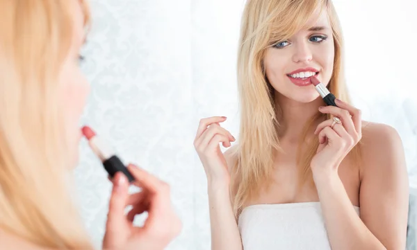 Mujer rubia sonriente aplicando lápiz labial en el espejo — Foto de Stock