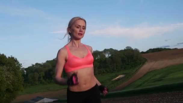 Ładna blondynka biegnie i ćwiczy na boisku podczas zachodu słońca — Wideo stockowe
