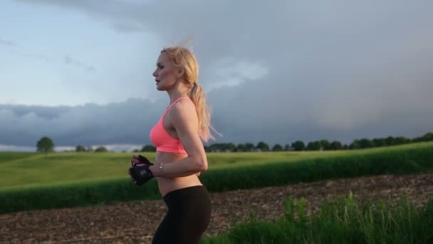 Bonita mujer rubia corriendo y haciendo ejercicio en el campo durante el atardecer — Vídeos de Stock