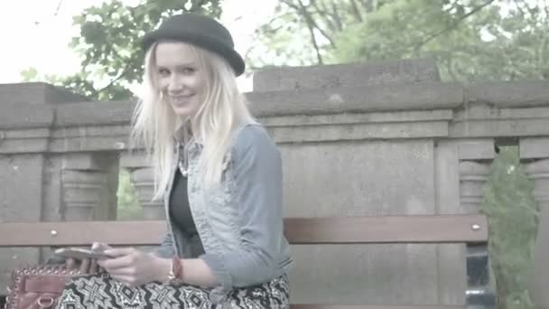 Atrakcyjny blond wysyłanie SMS-ów, siedząc na ławce — Wideo stockowe