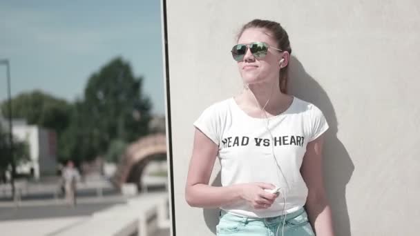 Retrato de una chica divertida en la playa escuchando música en auriculares desde el reproductor de mp3 de teléfonos inteligentes. en la ciudad — Vídeo de stock