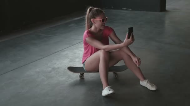 Jolie jeune femme skate prenant un selfie d'elle-même avec son téléphone intelligent dans le parking — Video