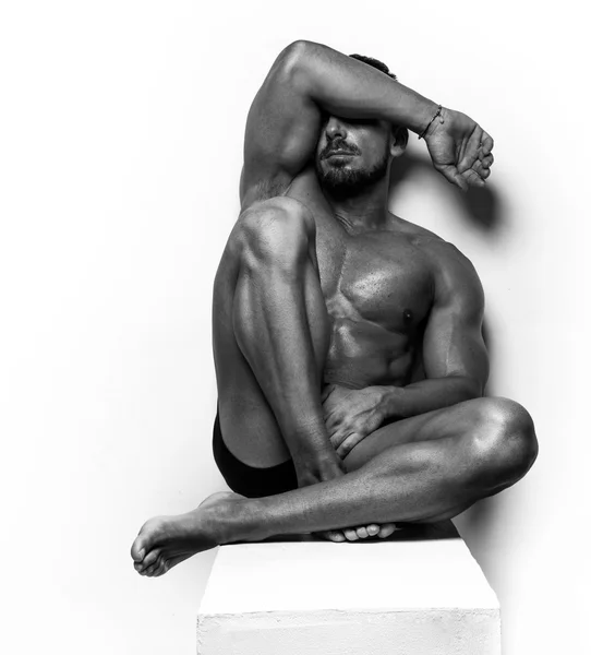 Muskulöser Mann sitzt auf weißem Grund — Stockfoto