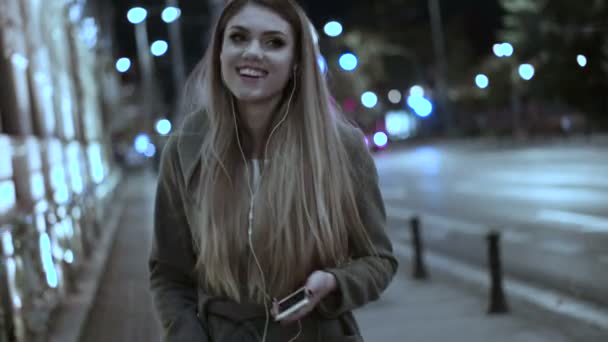 Mujer escuchando música en el teléfono celular caminando por la noche — Vídeos de Stock