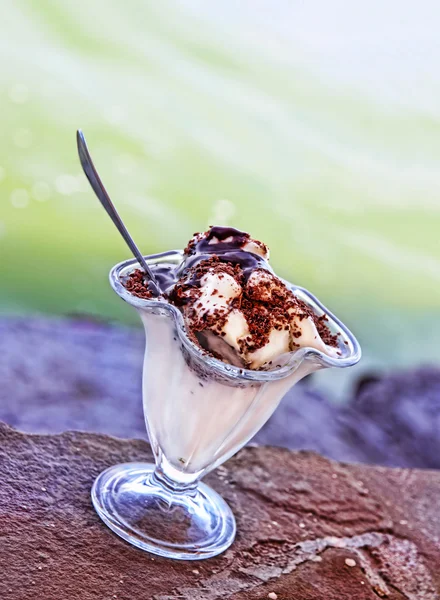 Ice cream topped with chocolate syrup on blurry sea wave backgro — Stock Photo, Image