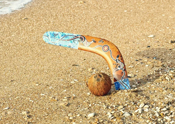 Boomerang en een kokosnoot op het zandstrand in de buurt van zee surf. — Stockfoto