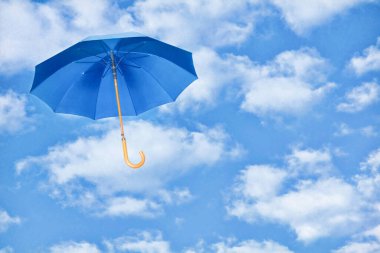 Mavi şemsiye beyaz bulutlara karşı gökyüzünde uçuyor. Değişim rüzgarı kavramı. Mary Poppins Şemsiyesi..