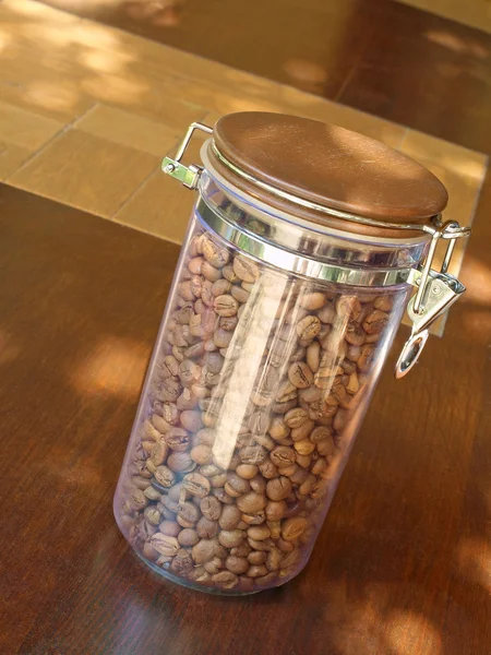 Coffee beans in glass container on wooden table. — Stock Photo, Image