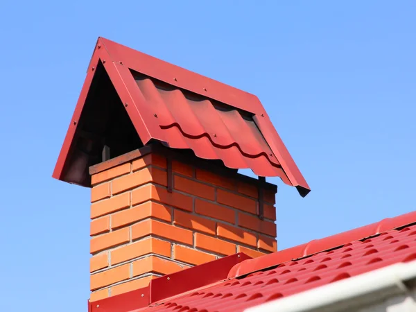 Brick chimney on a red tiled roof taken closeup against of blue — Stock Photo, Image