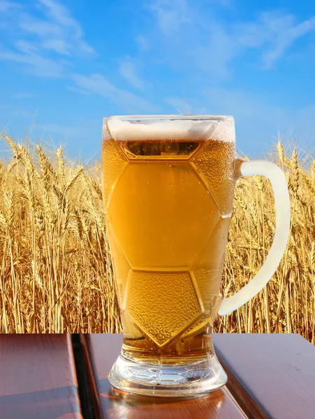 Vaso de cerveza sobre mesa de madera contra de trigo y cielo . — Foto de Stock