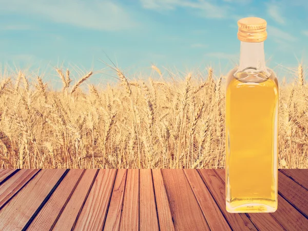 Vegetable oil on wooden table on wheat ears and blue sky backgro — Stock Photo, Image