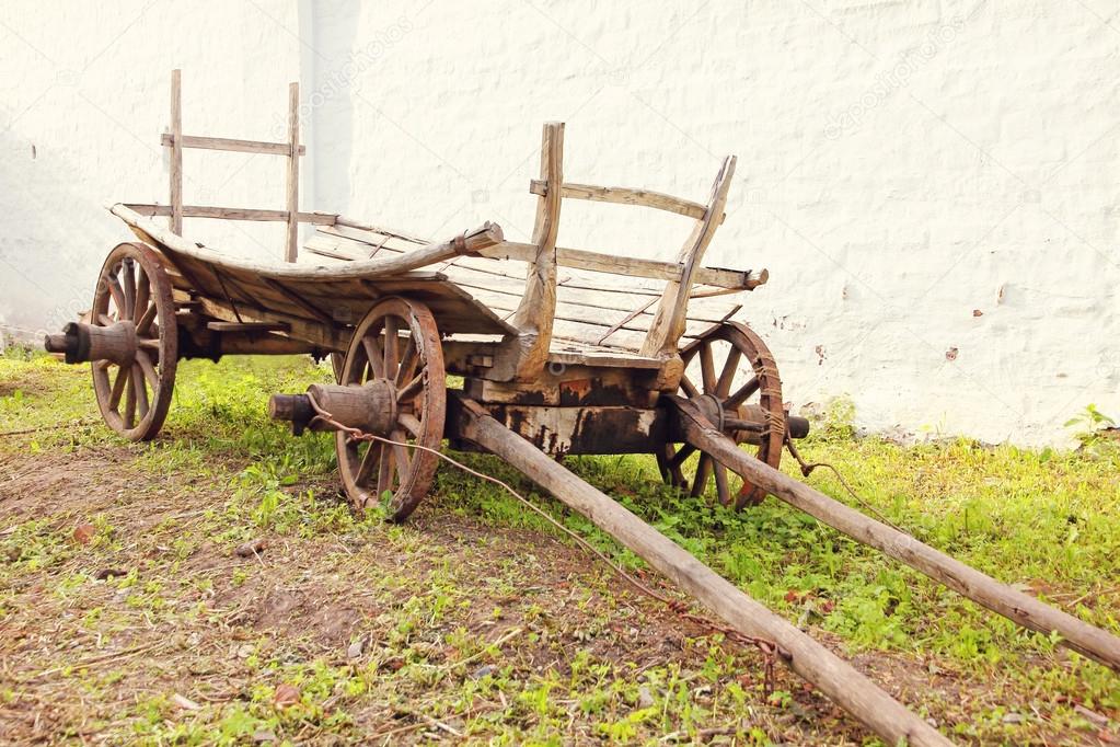 Vintage old rough wooden cart in front of old clay wall.