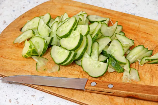 Fresh sliced cucumber and knife on wooden cutting board. — Stock Photo, Image