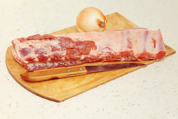 Costillas de cerdo crudas, cuchillo y cebolla en la mesa de la cocina . —  Fotos de Stock