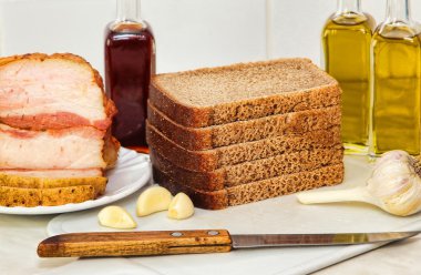 Beyaz mutfak masasında dilimlenmiş ekmek, pastırma ve zeytin yağı.