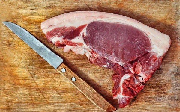 Carne de porco crua e faca na placa de corte de madeira . — Fotografia de Stock