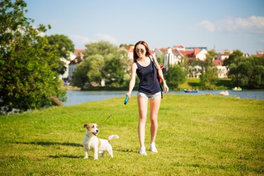 Köpeğiyle parkta yürüyen genç bir kadın.