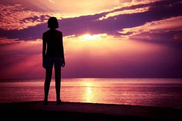 Silhouette einer jungen Frau, die den Sonnenuntergang am Meer beobachtet — Stockfoto