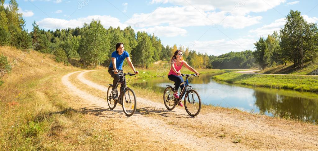 Young Happy Couple Riding Bicycles by the River