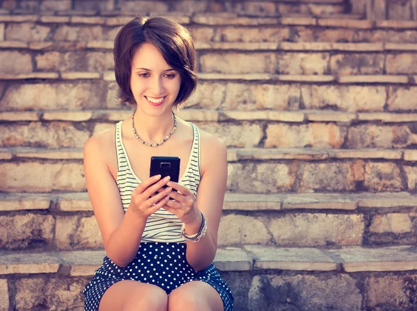 Улыбающаяся хипстерша пишет смс со своего мобильного телефона — стоковое фото