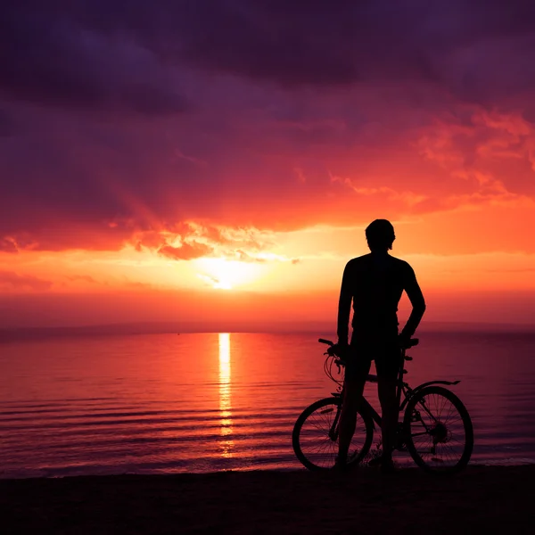 男人站与一辆自行车在日落在海边 — 图库照片
